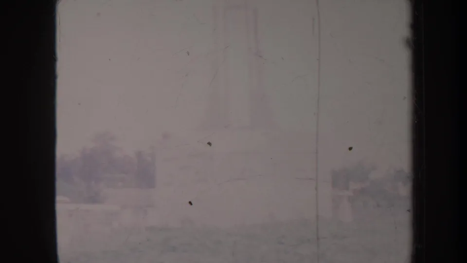 1967 Honolulu home-movie frame showing a hazy landscaped area with distant trees, low structures, and railings partly obscured by film wear.