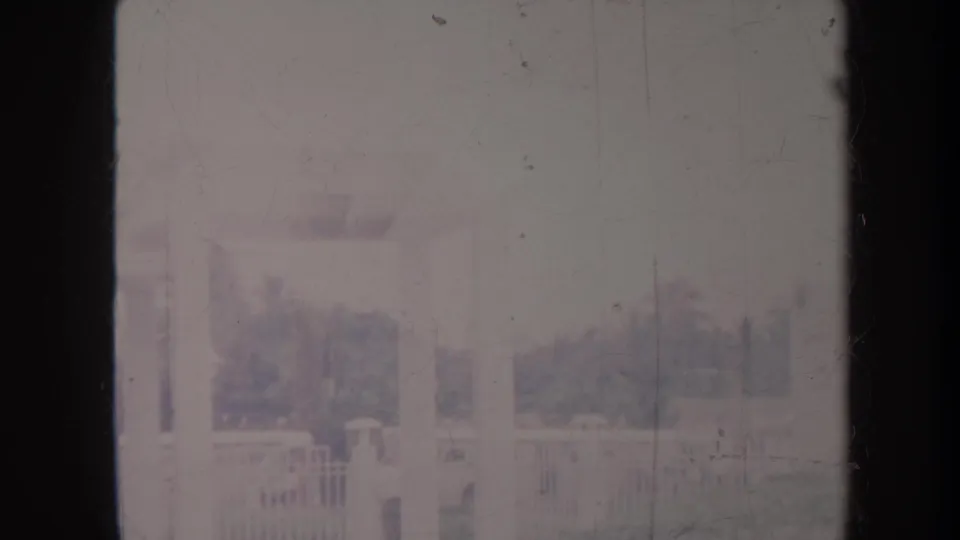 Hazy Honolulu garden scene with trees, fencing or railings, and a faint upright structure visible through faded 8mm film texture.