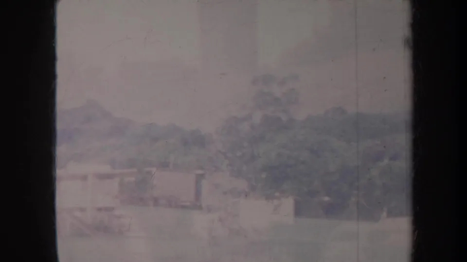 Faded 1967 Honolulu airport-side view with low structures, trees, and grass seen in soft home-movie focus.