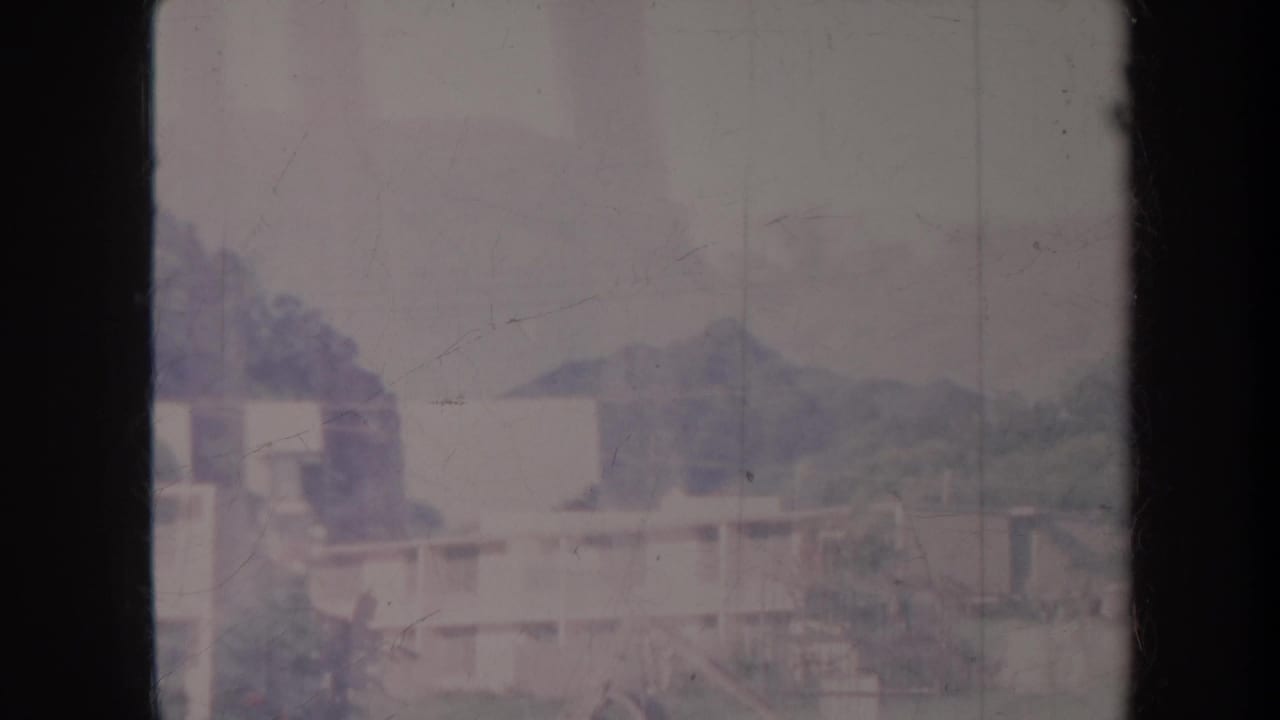 Soft, overcast view of rooftops, trees, and hills behind a dark center film edge.