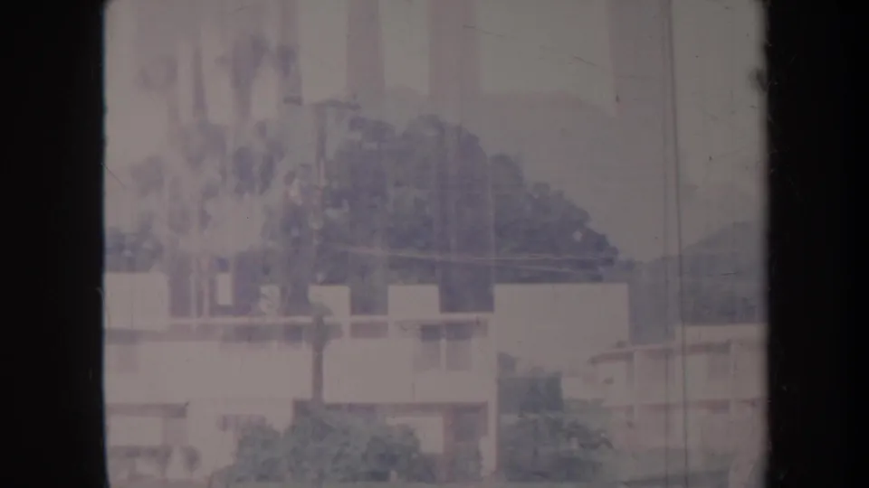 1967 Honolulu home-movie view of low building walls, trees, and hazy hills, with visible scratches and faded 8mm color.