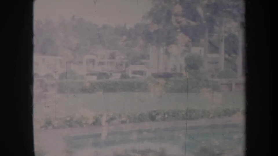 Faded 1967 Honolulu home-movie frame showing a landscaped park area with lawn, trees, pale structures, and distant buildings.