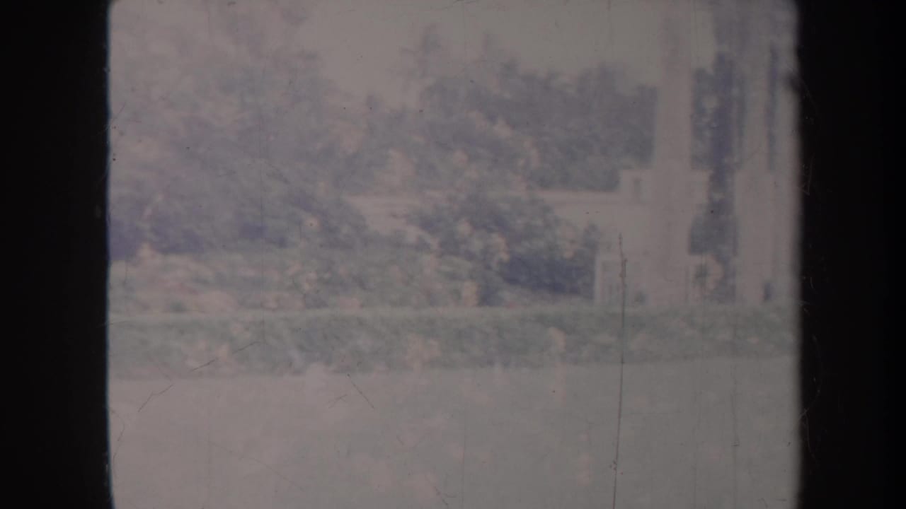 Faded 1967 Honolulu park frame showing trees, shrubs, lawn, and pale structures near the edge of the handheld pan.