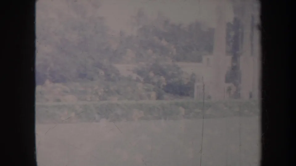 Faded 1967 Honolulu park frame showing trees, shrubs, lawn, and pale structures near the edge of the handheld pan.