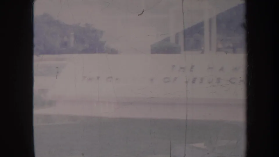 1967 Honolulu 8mm frame showing a pale Latter-day Saints church exterior with signage, roofline, columns, lawn, and soft faded color.