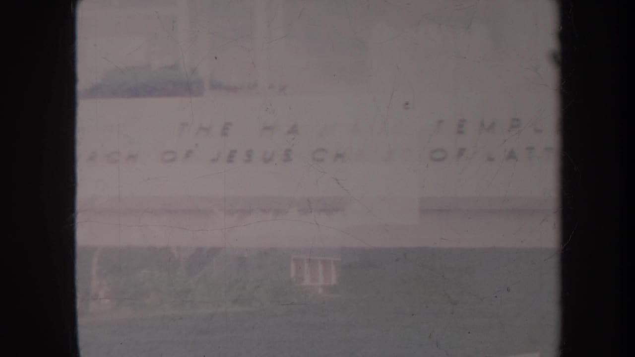 Pale church facade with lettering across the building and a lawn in front.
