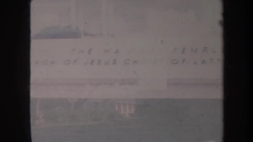Faded 1967 Honolulu frame of the church facade, showing broad lettering, a pale roofline, lawn, trees, and visible film wear.