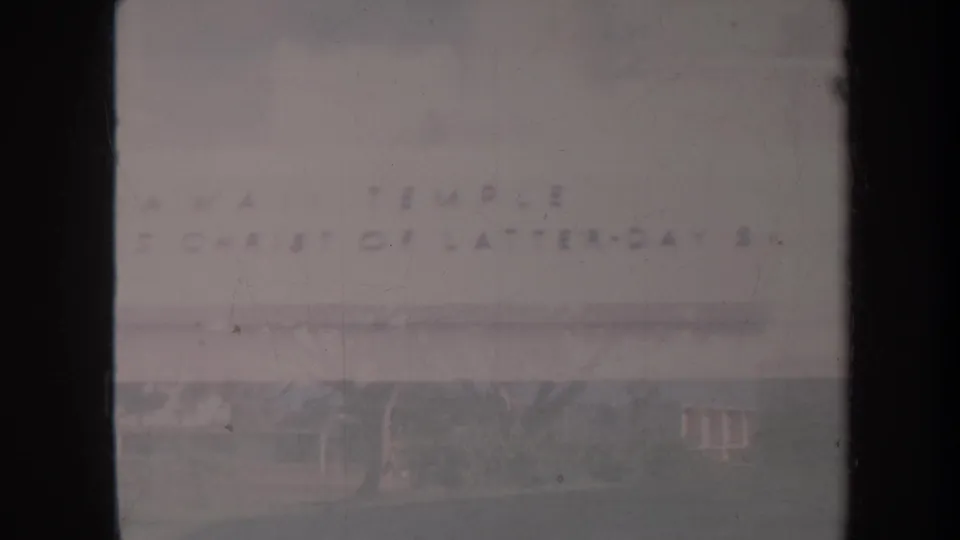1967 Honolulu 8mm frame with soft, washed lettering on a church exterior, foreground lawn, nearby trees, and dark contact-sheet borders.