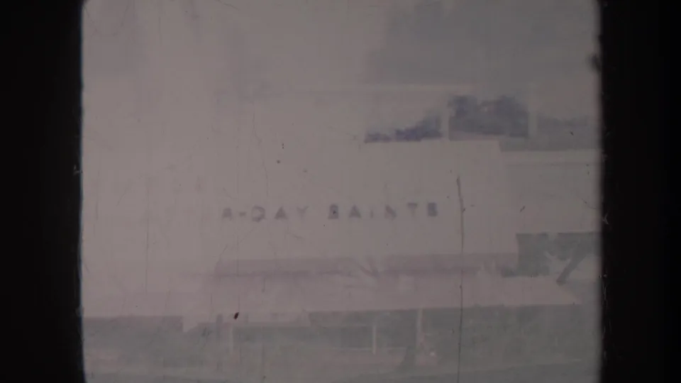 Final 1967 Honolulu frame showing part of the church exterior and signage, with roofline, lawn, trees, and pronounced 8mm fading.
