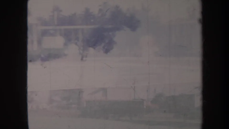 1967 Honolulu home-movie view of a hazy street with palm trees, low houses, and a dark window edge from a moving viewpoint.
