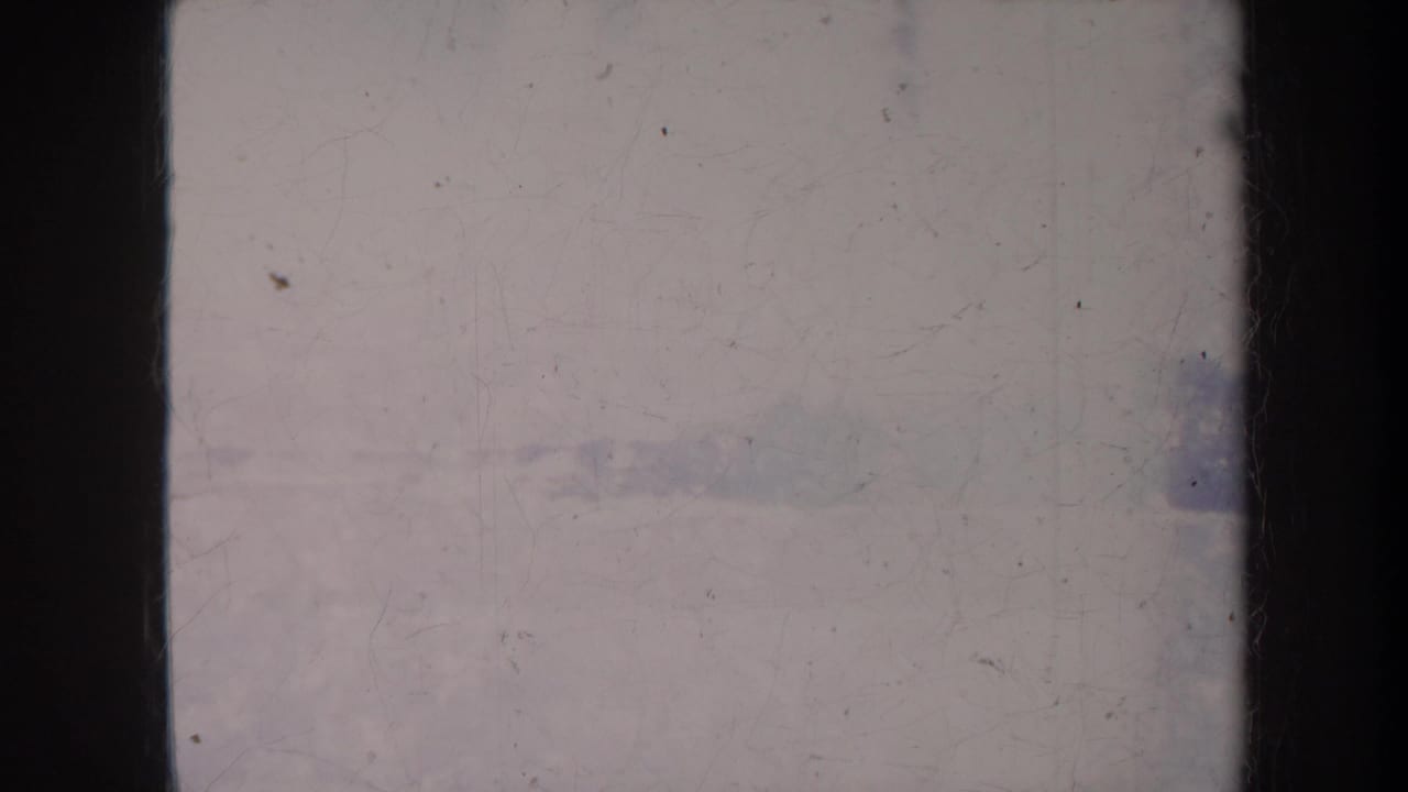 Soft, faded view through dark vertical bars toward pale sky, distant greenery, and low rooftops.