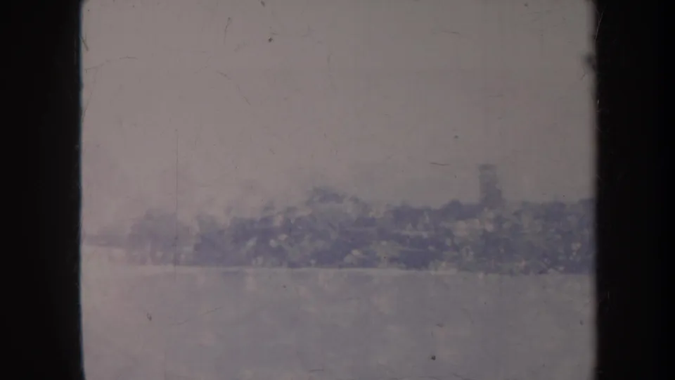 Faded 8mm Honolulu frame looking past a dark vertical divider toward distant greenery and a hazy sky.