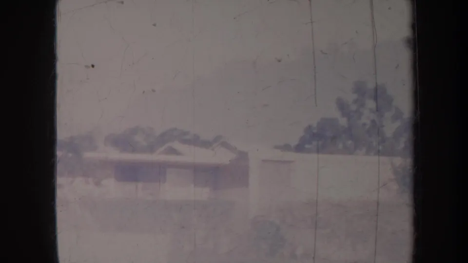 Faded 8mm Honolulu frame showing low houses, trees, and dark foreground bars, with no readable signs or logos.