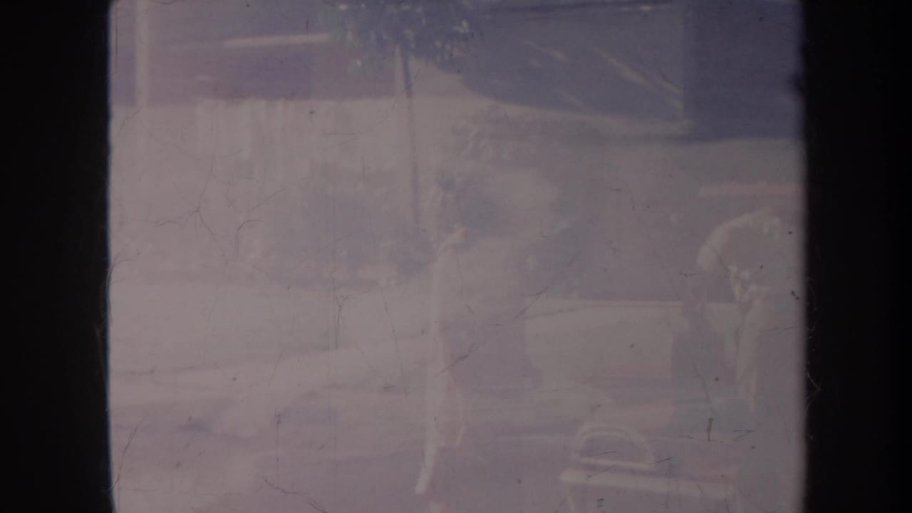 Faded Honolulu vacation frame with a person near a vehicle and palm-like foliage visible through heavy 8mm wear.