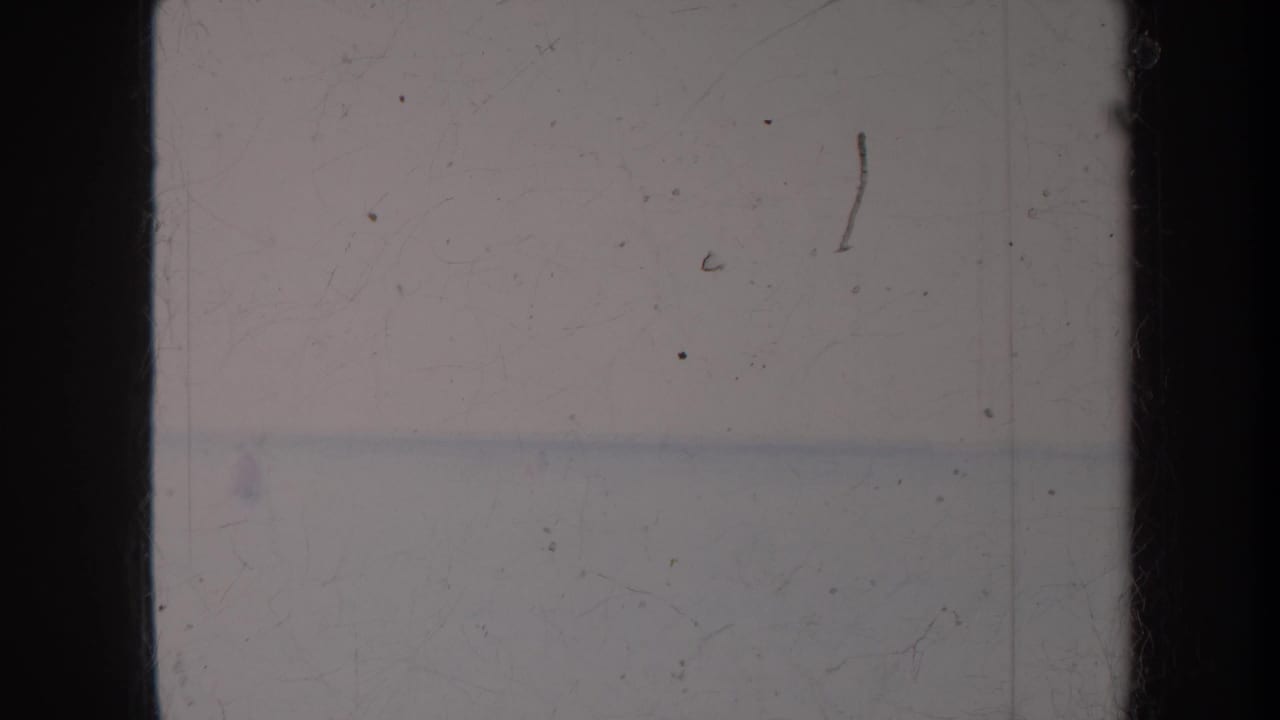 Pale ocean and sky divided by a faint horizon, framed by dark film borders.