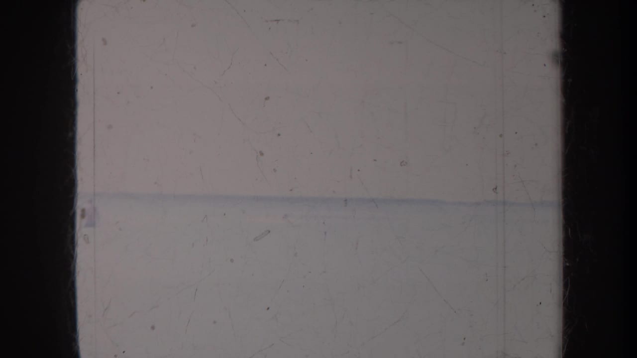 Soft ocean horizon and bright sky with visible dust and a dark vertical film border.