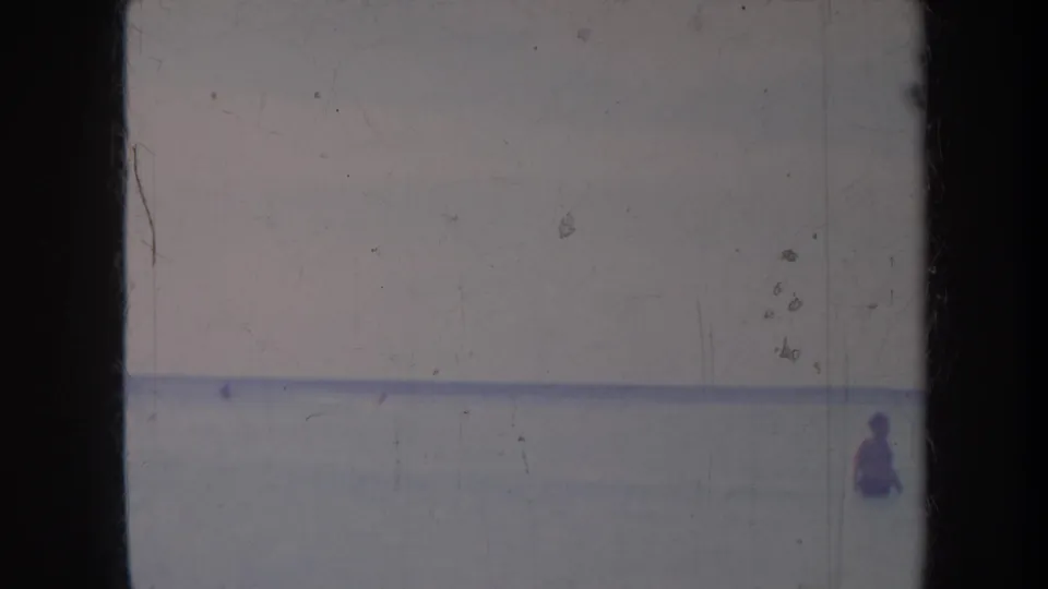 1967 Honolulu home-movie frame with a small distant figure wading in ocean water below a hazy horizon.