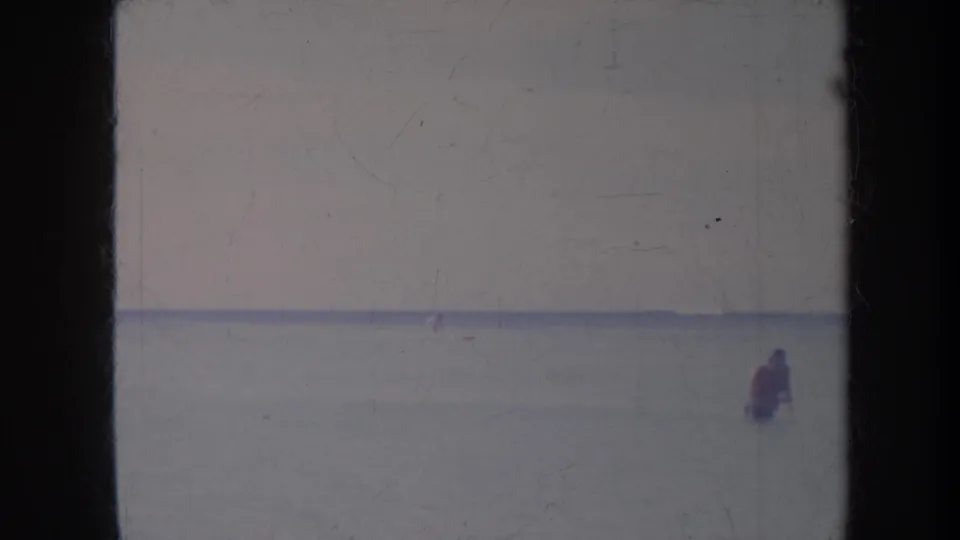 1967 Honolulu home-movie frame with a distant figure in calm blue ocean water under a pale horizon.