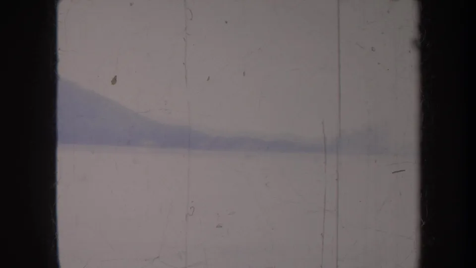 Faded 8mm view of a Honolulu-area shoreline and low mountain ridge across calm water, with vertical film marks.