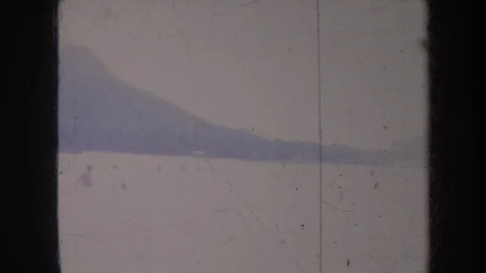 1967 Hawaii 8mm frame with a mountain slope, shoreline, and calm water rendered in faded purple-blue tones.