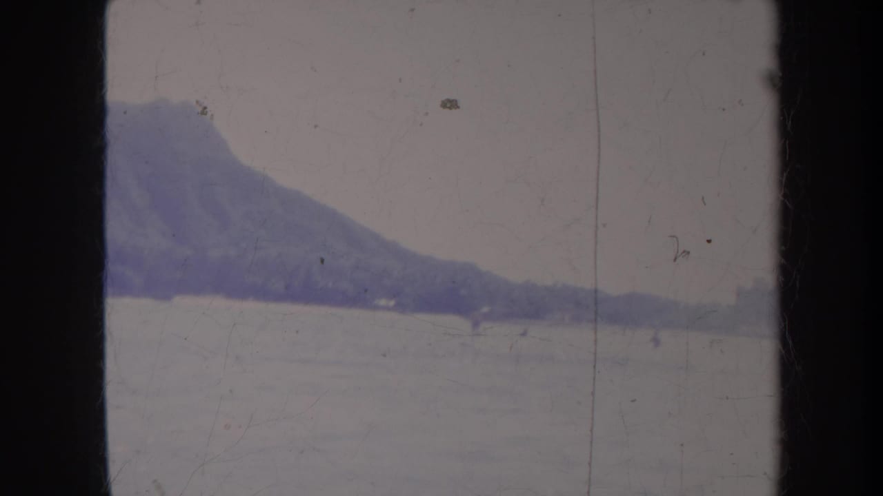Diamond Head rises behind pale ocean water with distant figures on the surface.