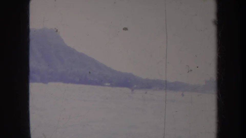 1967 Honolulu home-movie frame showing Diamond Head beyond bright ocean water and small distant water-skiing figures.