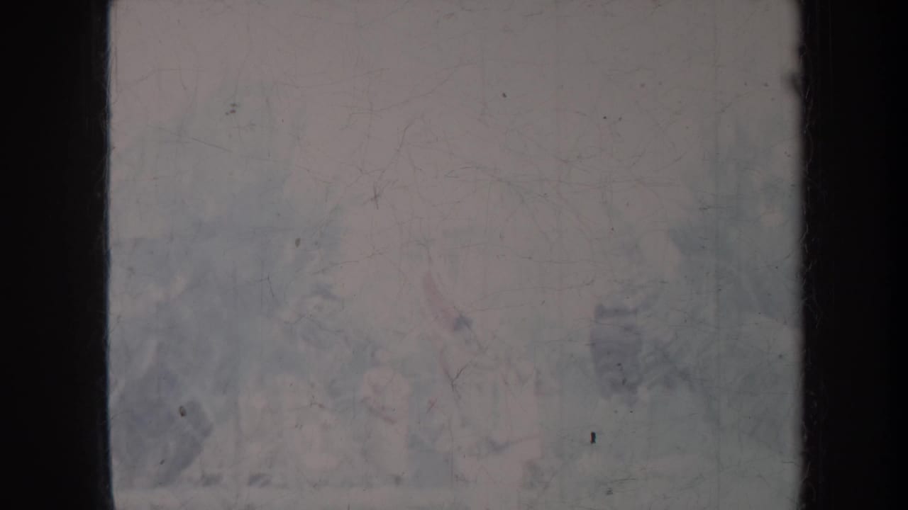 Faded scratched film frame with dark vertical edges and indistinct pale shapes.