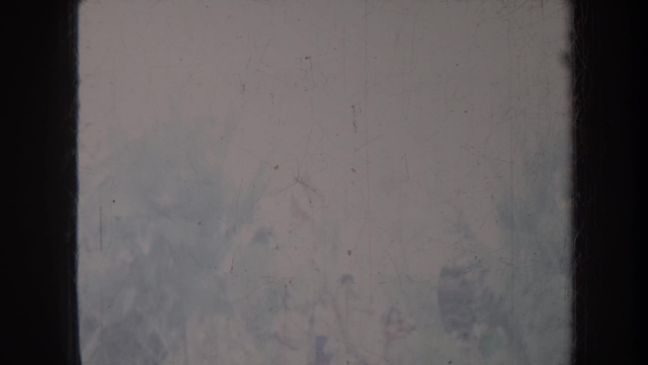 Soft faded frame with central dark border, scratches, dust, and blurred pale detail.