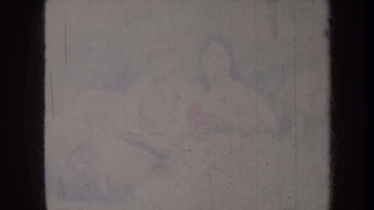 Faint seated figures obscured by dark frame bars and faded film wear.