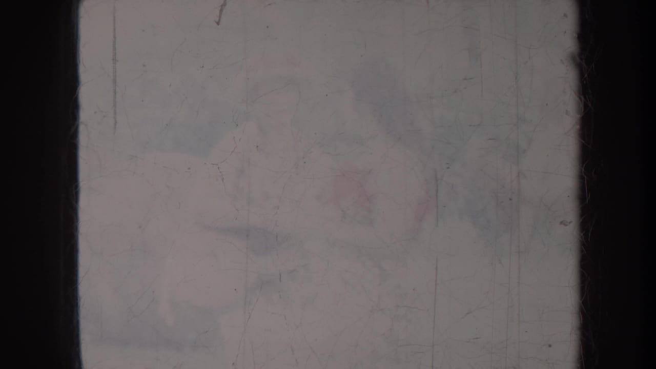 Faint outdoor scene behind dark film borders and heavy scratches.