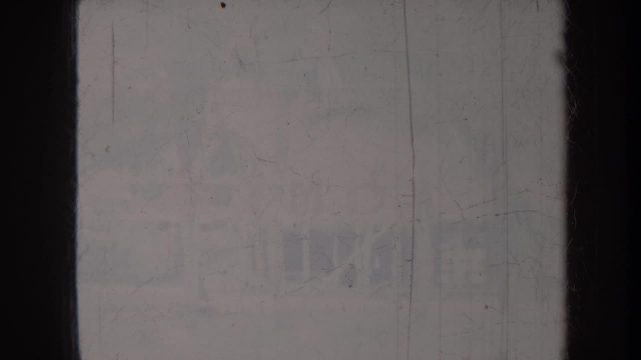Washed-out outdoor view with scratches, dark frame edge, and faint shapes.