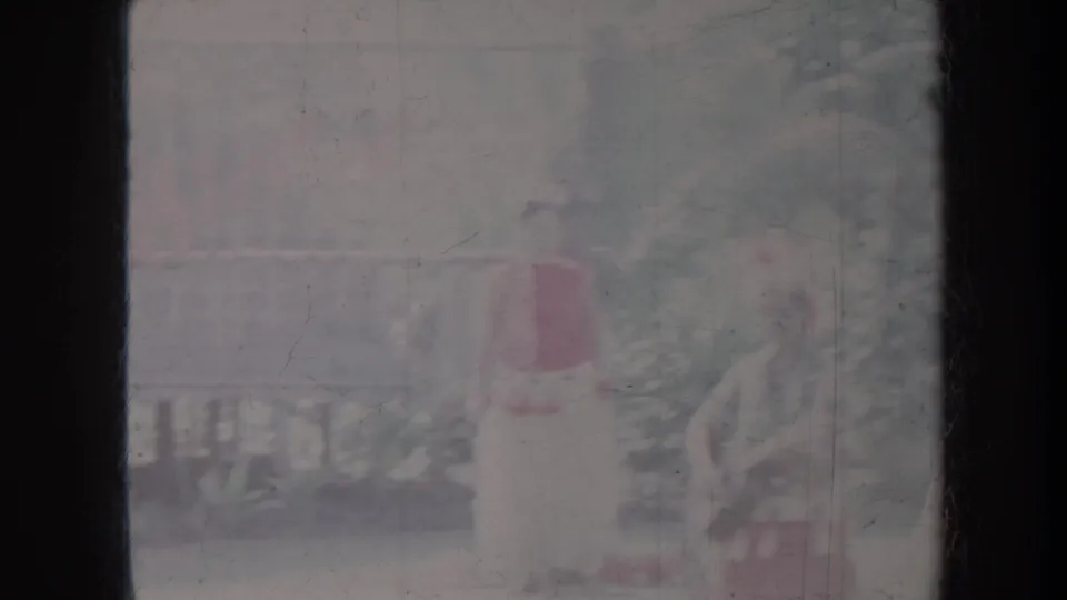1967 Honolulu home-movie frame showing a hula performer in red and white costume, softened by overexposed 8mm film.
