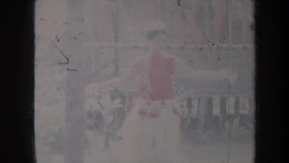 A 1967 Honolulu home-movie still shows a hula dancer mid-performance, partly obscured by overexposure and film scratches.