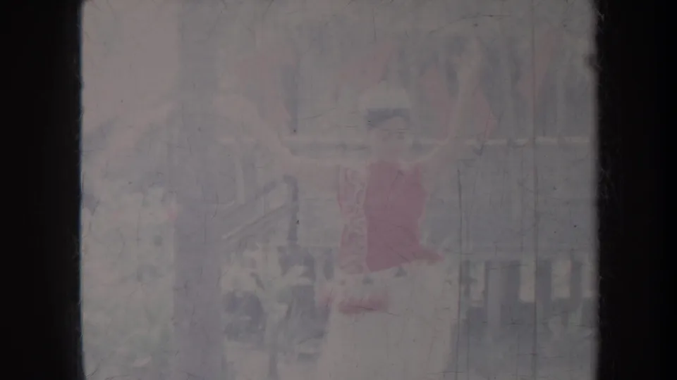 Final 1967 Honolulu frame showing a hula performer in red against porch railings and a tropical backdrop.