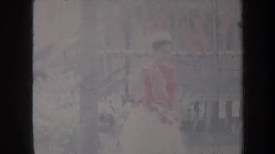 1967 Honolulu home-movie frame showing a young dancer in red and pale dress outdoors, softened by faded 8mm exposure.