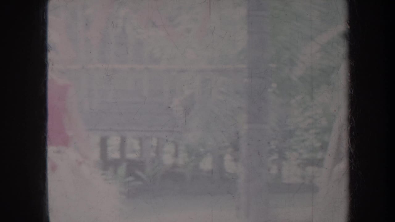 Soft, faded outdoor view with railings, greenery, and indistinct people in the background.