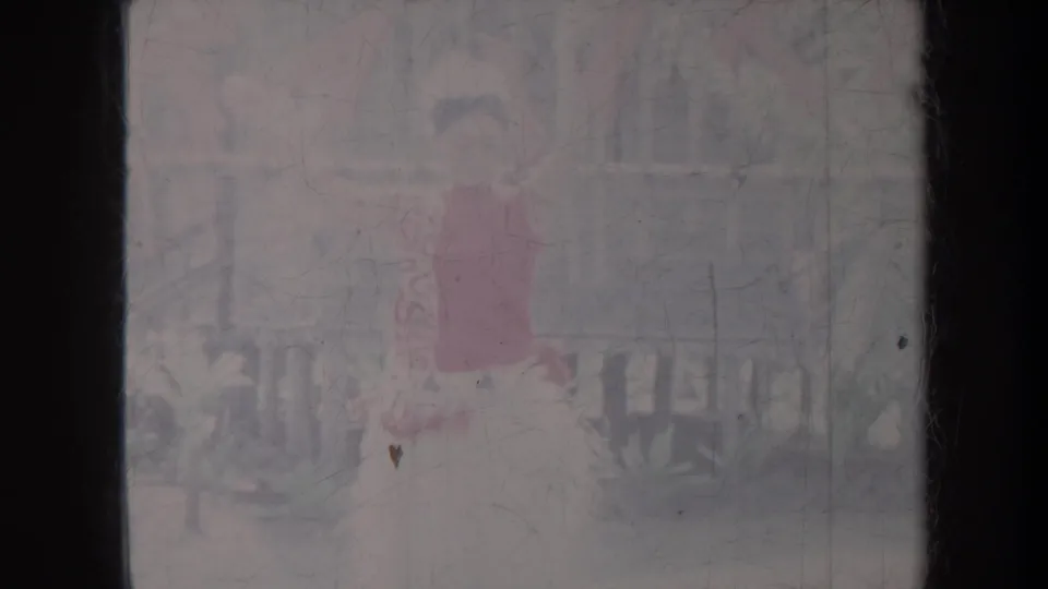1967 Honolulu home-movie frame showing the dancer in red skirt near railings and tropical plants during the hula sequence.