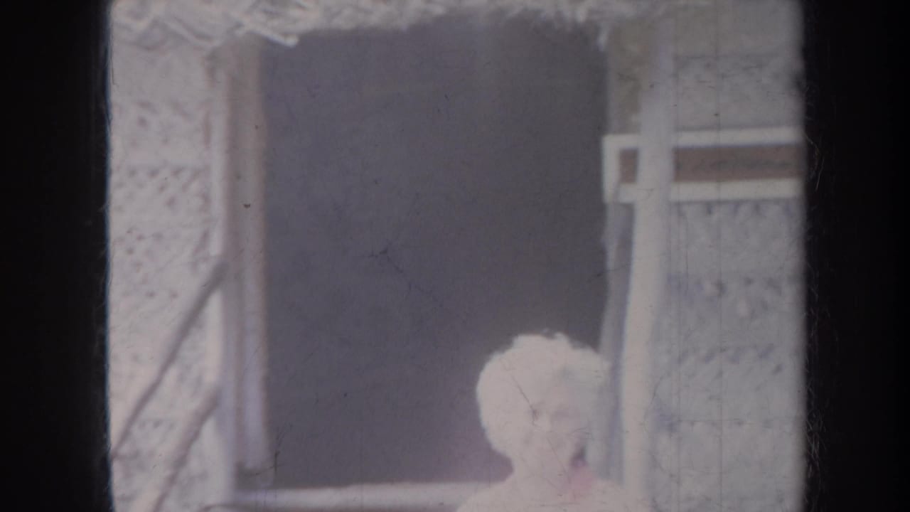 Adult with short light hair near a thatched structure and lattice wall.