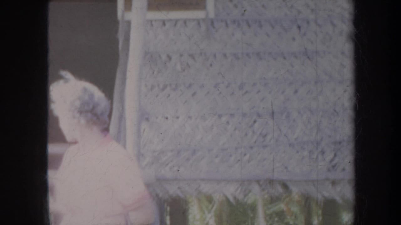 Woman in a light dress standing beside a woven wall panel.