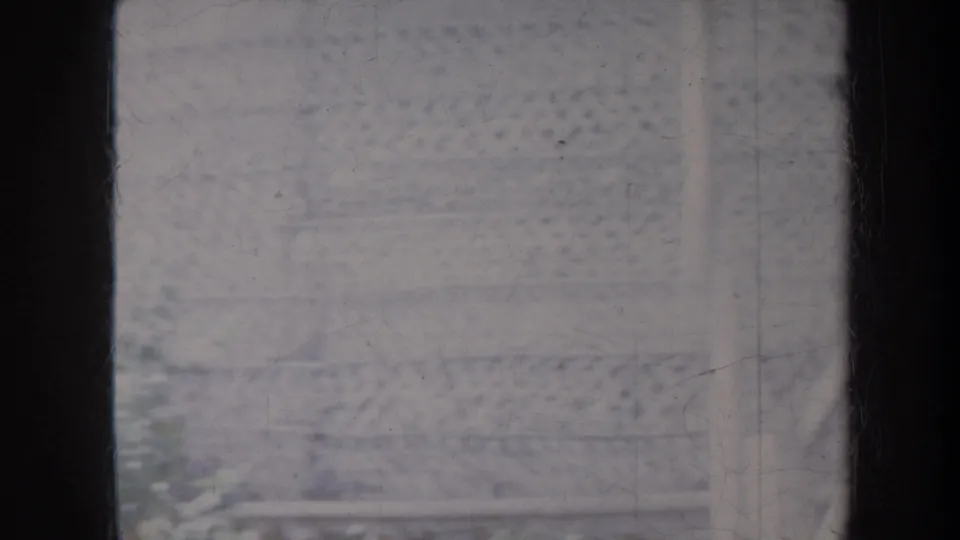 A faded 1967 Honolulu home-movie frame showing parts of a thatched structure, lattice panels, and heavy film wear.