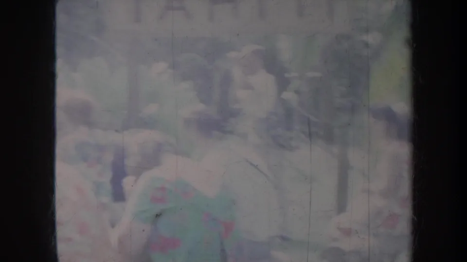 Tourists at a Honolulu tropical resort appear in faded 1960s home-movie footage, with hats, dresses, and foliage visible behind dark film edges.