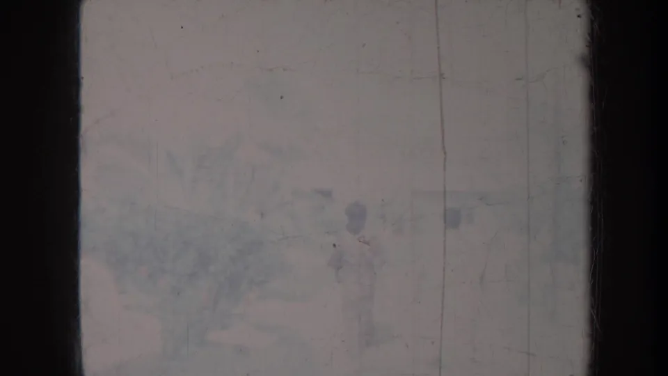 Heavily faded Honolulu home-movie frame with a distant standing figure near landscaping in an outdoor setting.
