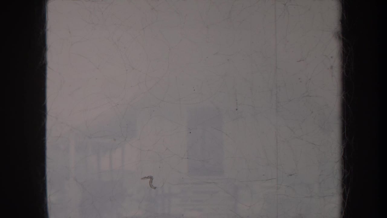 Faded frame with a seated guitarist and a standing dancer barely visible through film wear.