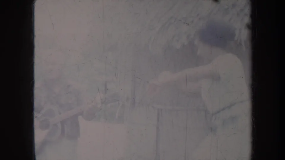 Home-movie frame from Honolulu in 1967 showing the dancer in motion near the guitarist, softened by aged 8mm exposure and scratches.