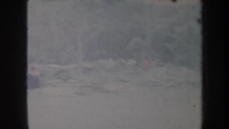 Blurred 1967 Honolulu home-movie frame showing a distant person near scattered pale logs or debris in a faded outdoor setting.