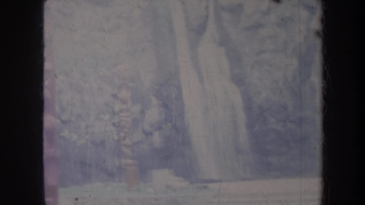 Dark cliff face and wooded shapes with a pale vertical waterfall-like form near the center.