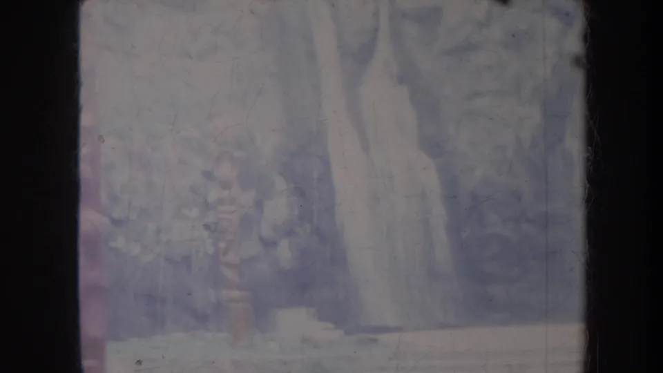 1967 Honolulu travel footage frame with a dark rocky backdrop, trees, and a pale vertical waterfall form during a handheld pan.