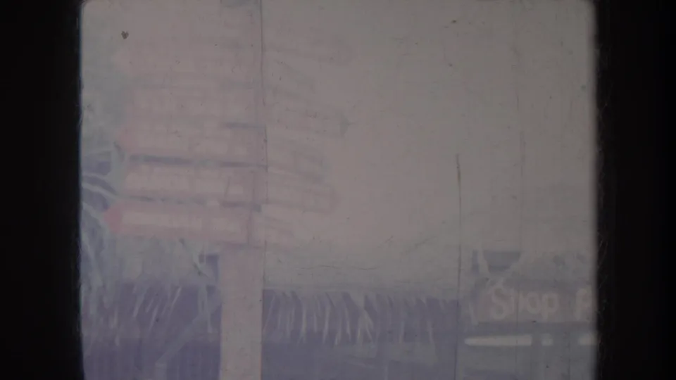 Faded 8mm Honolulu frame showing a soft street view with a signpost, plants, and partially visible storefronts.