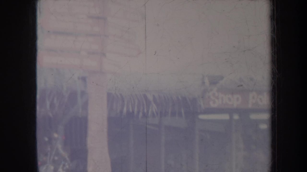 Soft view of a tropical shopfront partly obscured by dark window borders and film wear.