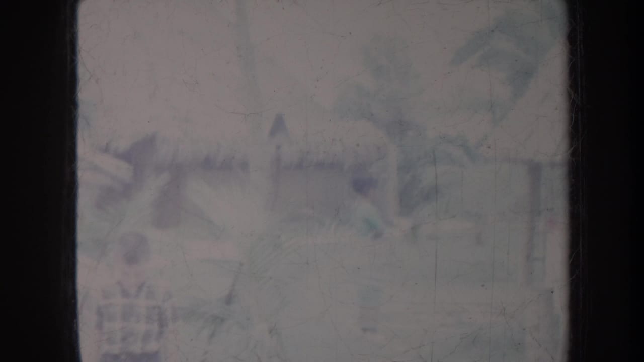 Soft tropical village view with palm trees, a distant figure, and hazy building shapes.